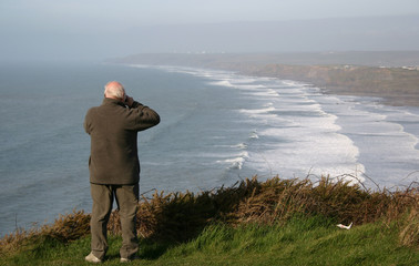 man on cliff-top taking a photo of the coast