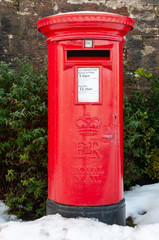 Fototapeta na wymiar A traditional red British Post Box in a snowy rural setting