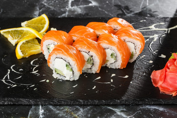 Sushi Rolls with cucumber, avocado, salmon and Cream Cheese inside on black slate isolated on black marble background. Philadelphia roll sushi. Sushi menu. Horizontal photo.