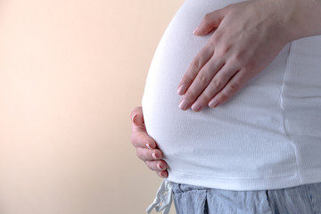 Authentic close up shot of an young pregnant woman in pajamas is caressing her belly just woke up in a bedroom in the morning.