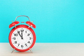 Red retro alarm clock with five minutes to twelve o'clock, on wooden table on a blue background. The concept of time, holiday, 5 minutes to the event, deadline. Layout with copy space for your text.