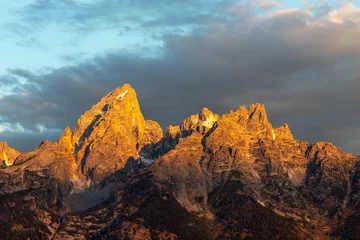 Acrylic prints Teton Range The golden peak of a mountain at sunrise  with dark clouds in the beackground
