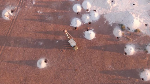 Aerial: Opal vacuum mine truck in a working mine in the outback region of Coober Pedy at sunrise. Heaps of mining sand visible in piles from excavated holes. Australia