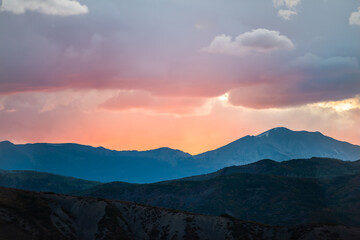 Naklejka na ściany i meble Orange red soft light cloudy sunset sun rays in Aspen, Colorado with rocky mountains peak and vibrant color of clouds at twilight with mountain ridge silhouette