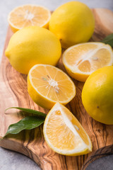 Naklejka na ściany i meble Fresh lemons in wooden bowl with leaves on grey stone background. Fresh fruits and slice flat lay. Citrus background, copy space