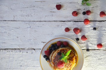 Pancakes with berries and maple syrup in a plate on a white wooden background