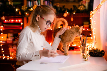 Adorable litle girl is writting a letter to Santa Klaus sitting on the table