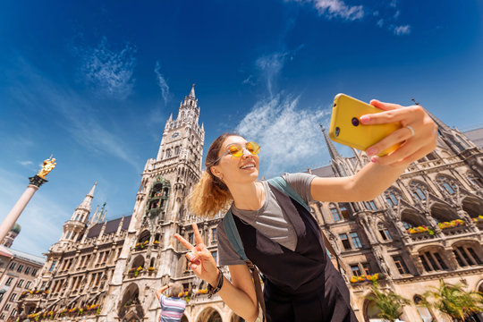 Cheerful Asian tourist girl takes a selfie on the background of Munich attractions to post photos on her blog and social networks