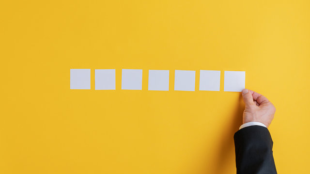 Hand of a businessman placing seven blank white post it papers in a row