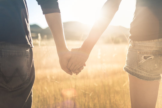 Young affectionate couple holding hands walking outdoors at sunset. 