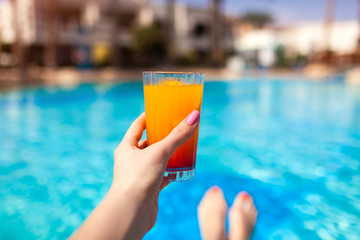Woman holds a cocktail on swimming pool background. All inclusive