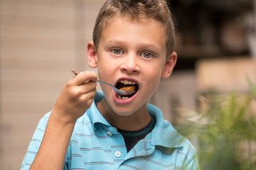 Boy eats with a spoon and laughs into the camera