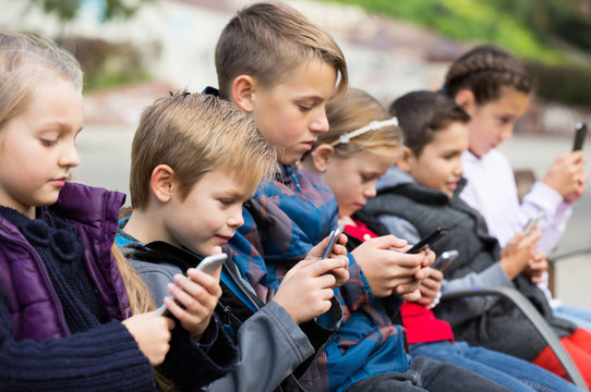 Children sitting on bench with smartphones