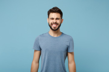 Young weird smiling man in casual clothes posing isolated on blue wall background, studio portrait. People sincere emotions lifestyle concept. Mock up copy space. Looking camera, Showing teeth.