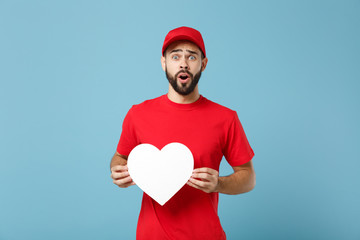 Delivery man in red workwear hold heart isolated on blue wall background studio portrait. Professional male employee in cap t-shirt print working as courier dealer. Service concept. Mock up copy space