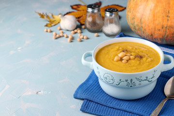 Vegetarian autumn pumpkin cream soup with chickpeas on light blue background, Closeup