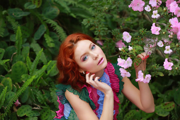 beautiful red-haired girl in arranger where azalea blooms in a colorful flying dress