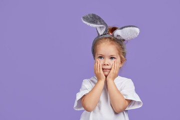 Portrait of cute smiling little child girl wears bunny ears on Easter day. Funny emotions on Violet isolated background