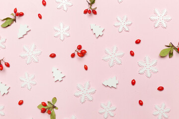 Elegant winter background. Red berries, snow flakes and little christmas tees on pale pink background. Christmas, winter holiday, new year concept.