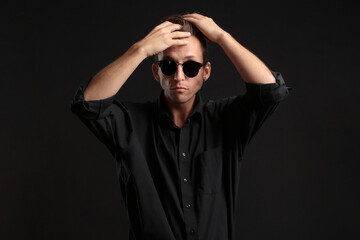 Confident stylish bussinesman in black eyeglasses fixing hair isolated over black background.