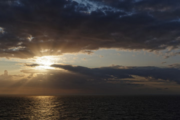 Fototapeta na wymiar Sun beams through clouds over the sea. Beautiful sunset scene.