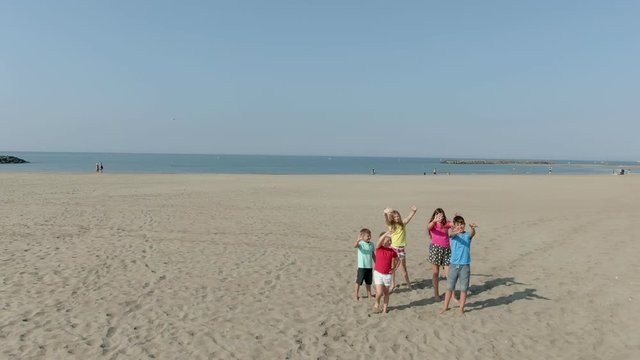 Five children in bright clothes wave their hands. Aerial shot of team of children on the beach