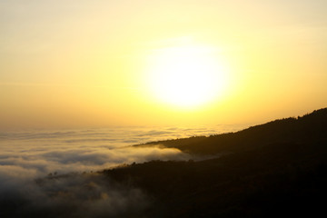 Fog covers the mountains during golden hour and a large ball of sun on the horizon