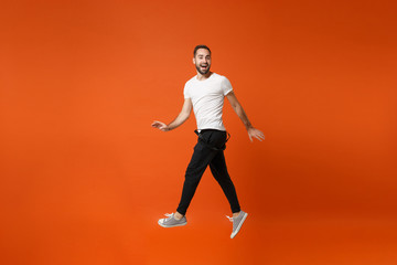 Fototapeta na wymiar Smiling funny young man in casual white t-shirt posing isolated on bright orange wall background studio portrait. People lifestyle concept. Mock up copy space. Having fun, fooling around, jumping.