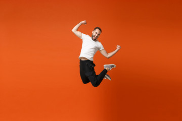 Happy joyful young man in casual white t-shirt posing isolated on bright orange wall background studio portrait. People lifestyle concept. Mock up copy space. Having fun jumping, doing winner gesture. - obrazy, fototapety, plakaty