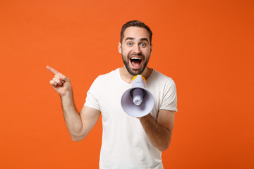 Excited young man in casual white t-shirt posing isolated on orange wall background. People sincere...