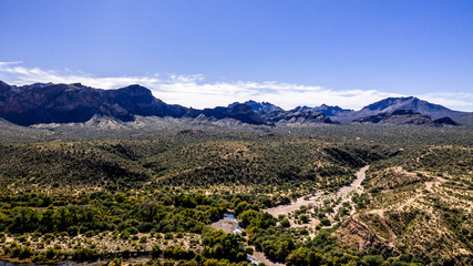 Fototapeta na wymiar Aerial, landscape along the Salt River in Arizona with pink and orange rocks, purple mountains, cool water, blue sky, cactus, green trees and brush on a Fall day