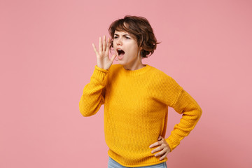 Displeased young brunette woman girl in yellow sweater posing isolated on pastel pink background studio portrait. People lifestyle concept. Mock up copy space. Screaming with hand gesture near mouth.