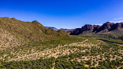 Fototapeta na wymiar Aerial, landscape along the Salt River in Arizona with pink and orange rocks, purple mountains, cool water, blue sky, cactus, green trees and brush on a Fall day