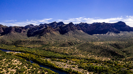 Aerial, landscape along the Salt River in Arizona with pink and orange rocks, purple mountains, cool water, blue sky, cactus, green trees and brush on a Fall day