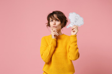 Pensive young brunette woman girl in yellow sweater posing isolated on pastel pink background....