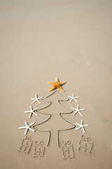 Eco-friendly Christmas tree decorated with starfish tree topper and simple presents drawn on the beach with smooth sand copy space