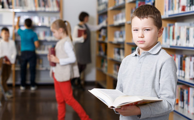 Tired boy looking for textbooks in library