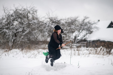Fototapeta na wymiar Excited girl dressed in with costume starting to gly on her broomstick to coven in snowy winter day in countryside nature.