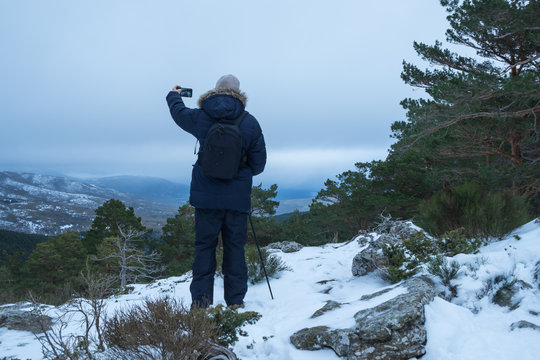 Middle-aged man, contemplating the snowy landscape on top of a mountain. taking pictures with his mobile phone.