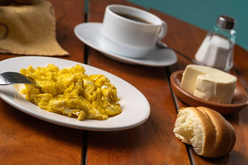 Breakfast with coffee, cheese and scrambled eggs, served on a wooden table, different types of bread and sweet empanadas with cheese