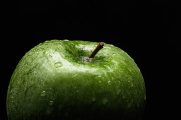 Appetizing green apple covered with drops of water on a black background. Close-up