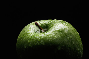 Appetizing green apple covered with drops of water on a black background. Close-up