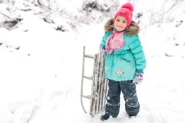 Lovely smiling girl with frozen sled in her hand posing for camera in winter snowy day outdoor.