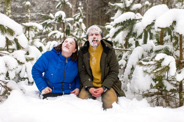 Obraz premium Portrait of funny couple with thier faces covered with snow standing on knnes in snowy forest