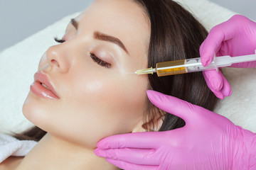 Cosmetologist does prp therapy on the face of a beautiful woman in a beauty salon. There is in vitro  blood plasma, ready for injection. Cosmetology concept.