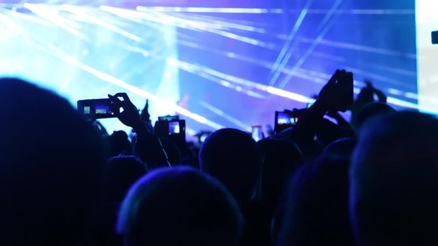 People waving hands with smartphones with flashlight. Live music concert. Happy people are watching an amazing musical concert. Fan taking photo of concert at festival. Handheld live video footage.