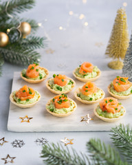Canapes with smoked salmon, cream cheese and avocado on light background with space for text. Christmas and new year holidays background concept. Starters snacks recipe ideas.