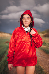 Young woman standing with raincoat and headphones on the field