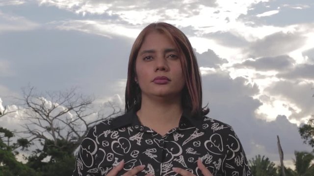 Close up shot of woman with hands on her breasts and staring straight ahead. Cloudy sky background.