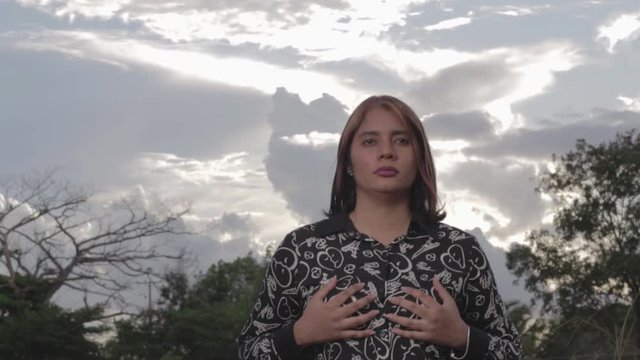 Slow motions shot of woman with hands on her breasts and staring straight ahead. Cloudy sky background.